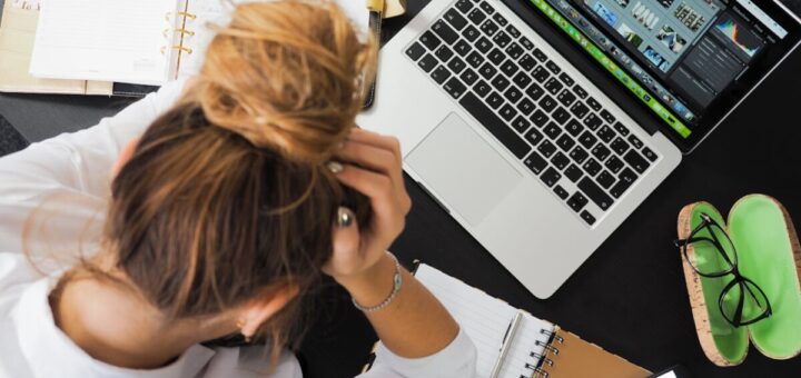 Overhead view of a stressed woman working at a desk with a laptop, phone, and notebooks.