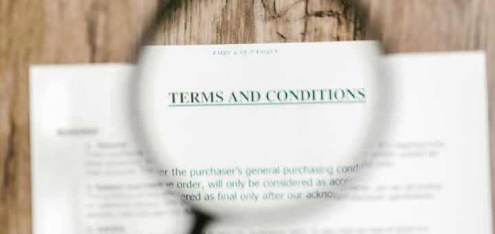 A magnifying glass held over a document with the heading "Terms and Conditions" in focus, emphasizing the text while the background appears blurred.